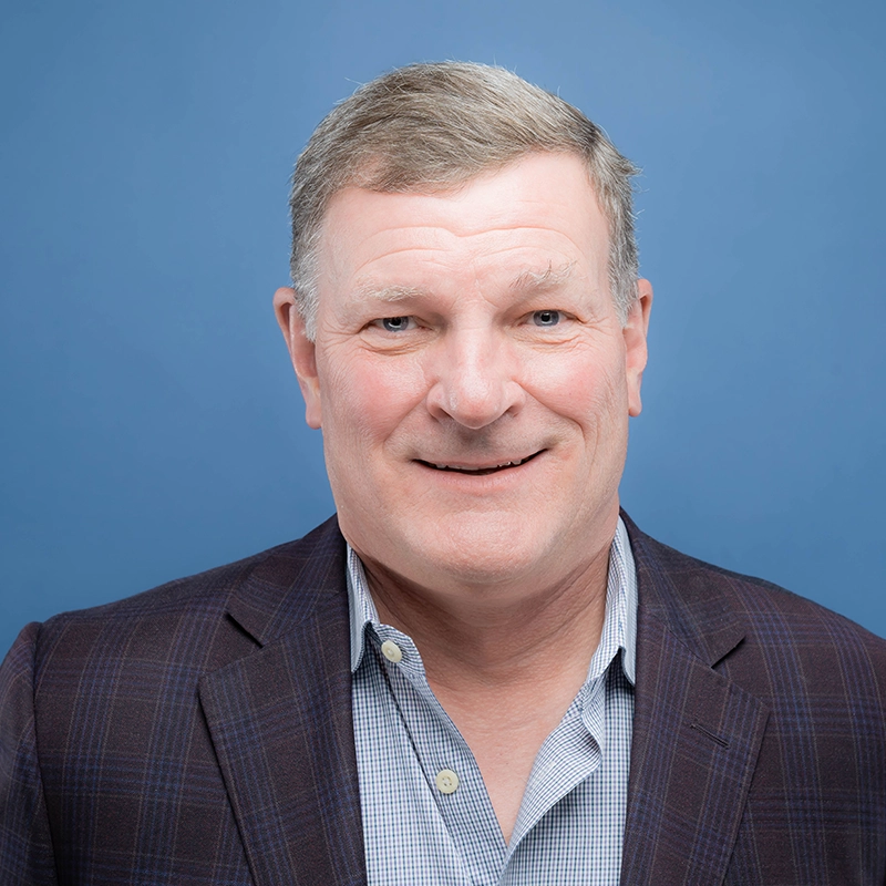 Brian Lemek smiles into the camera against a blue background.