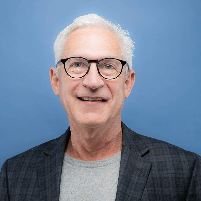 Jeff Bear smiles into the camera against a blue background.