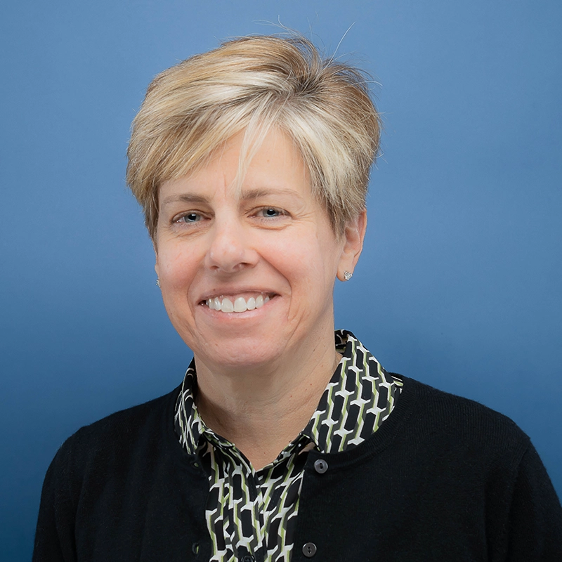 Laura Ekizian smiles into the camera against a blue background.