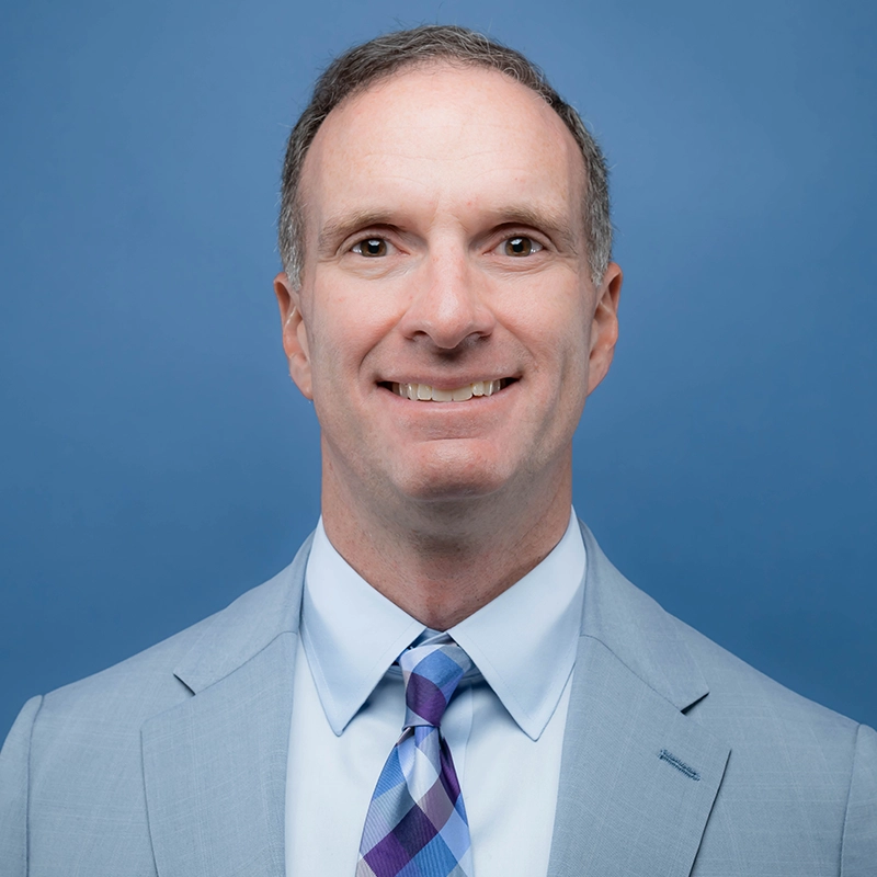 Paul Thompson smiles into the camera against a blue background.
