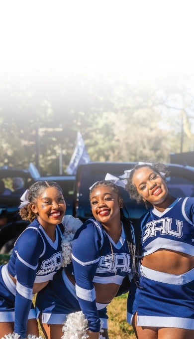 Three cheerleaders smiling together outside at homecoming tailgate.