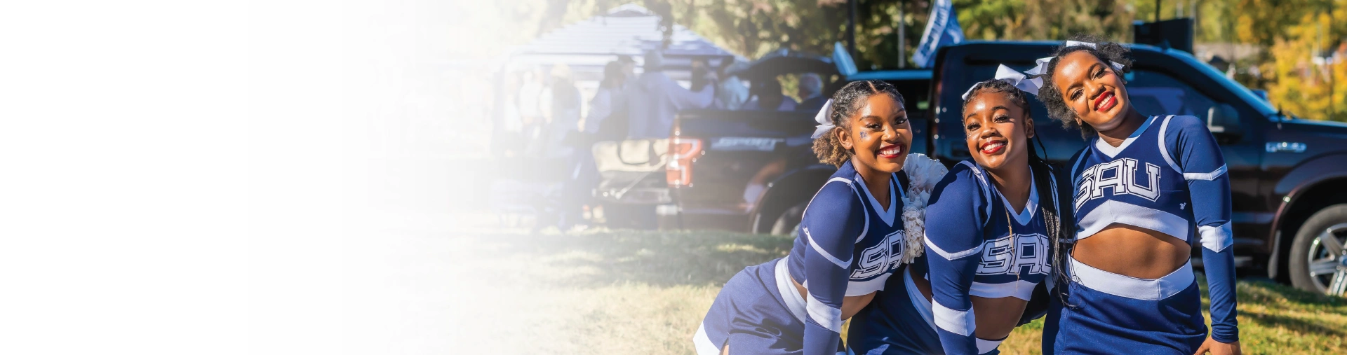 Three cheerleaders smiling together outside at homecoming tailgate.