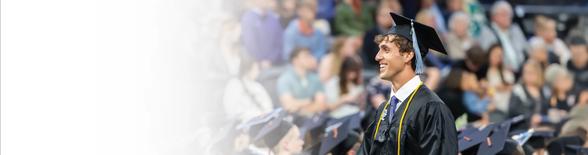 Graduate walking, smiling, amongst crowd at graduation ceremony.