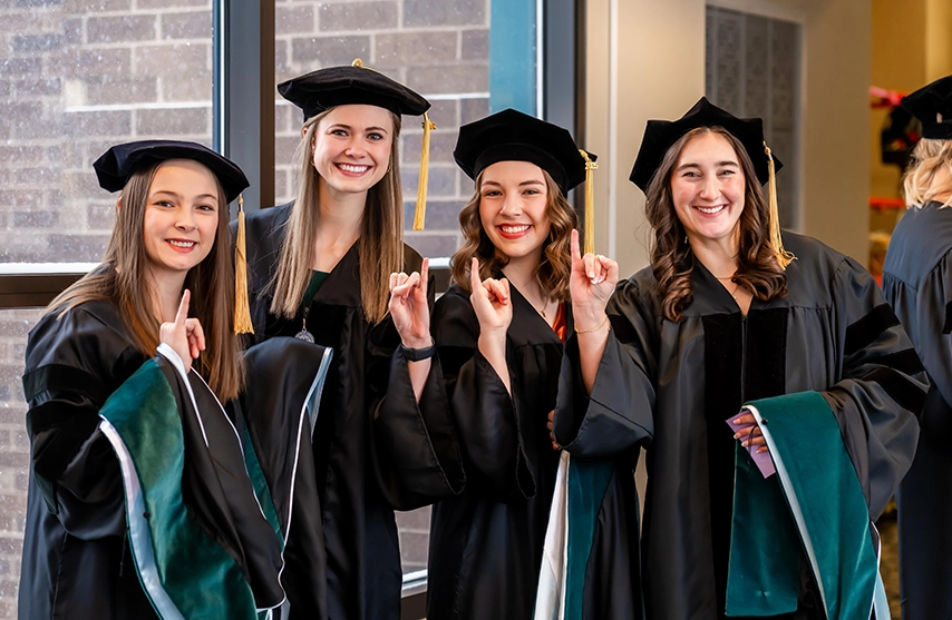 Four newly graduated students smile into the camera during St. Ambrose University's commencement in 2025.