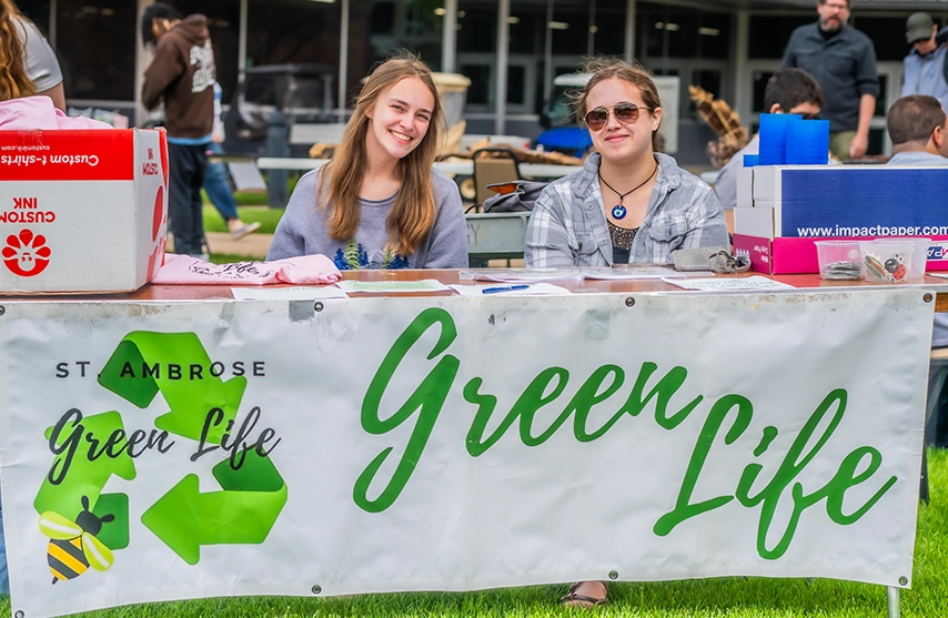 Two students sit together at a booth for SAU's Green Life group at SAU's Earth Day Festival.