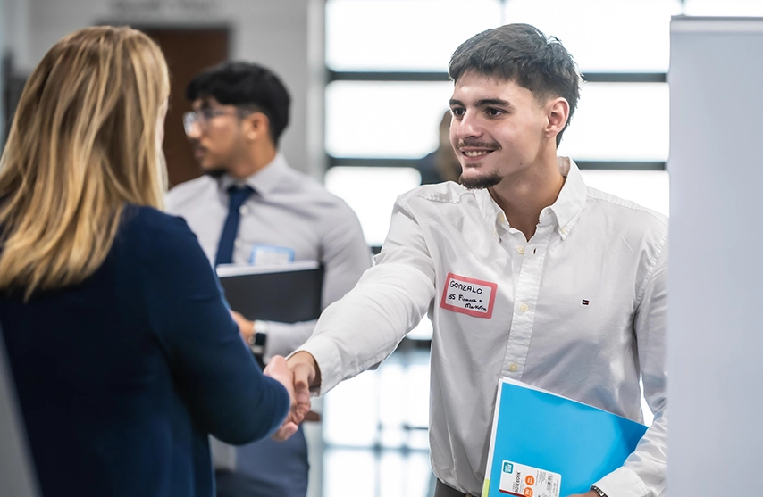 Student shaking hands with employer at networking fair.