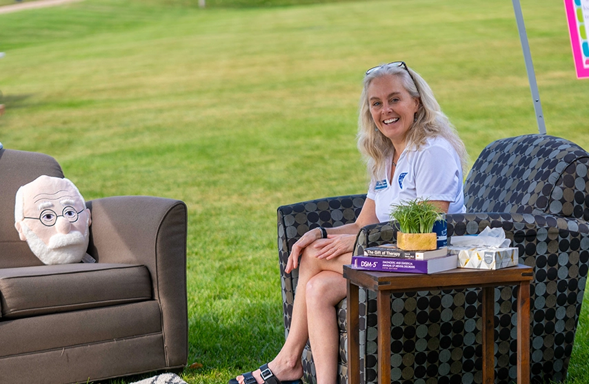 A St. Ambrose University counselor sits in a chair outside and smiles at the camera.