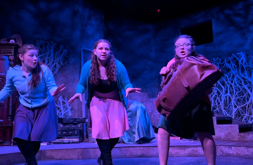 Three students couch on stage during a performance of Secret in the Wings.