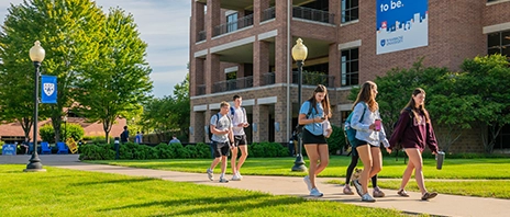Students walk along a campus sidewalk in front of the Rogalski Center.
