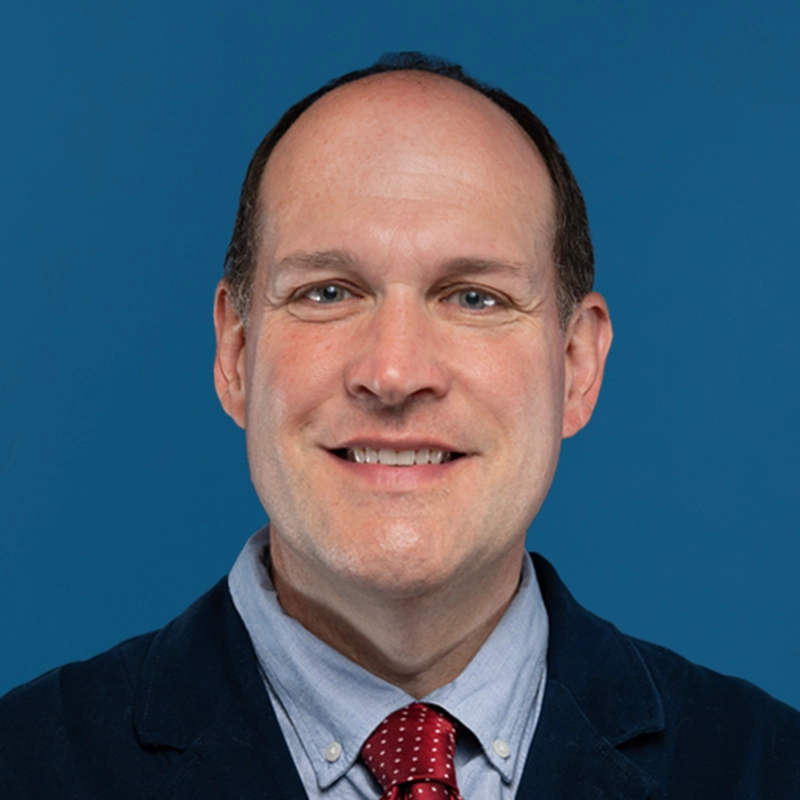 Ryan Heuer, PT, DPT, smiles into the camera against a blue background.