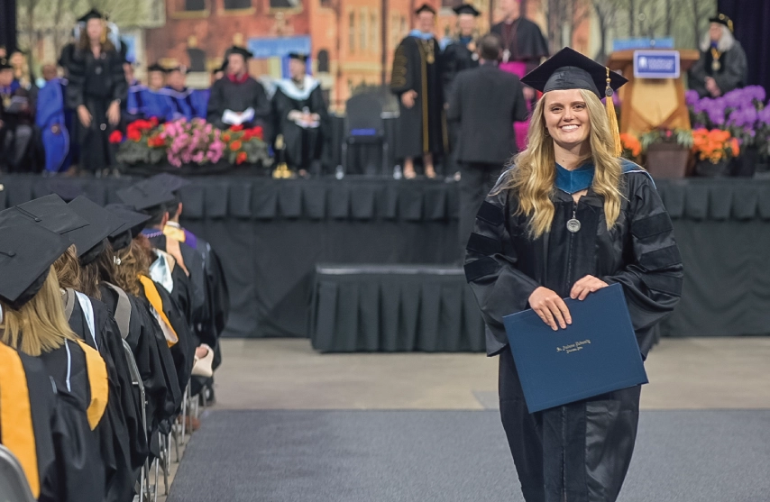 A smiling woman receiving her diploma at graduation.
