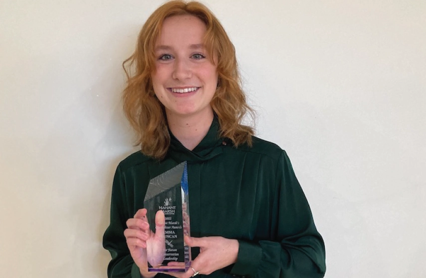 A young woman smiling and holding up an award.