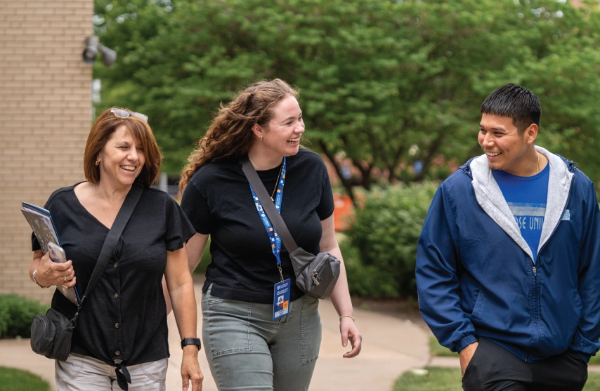 A group of 3 walking on campus and smiling.