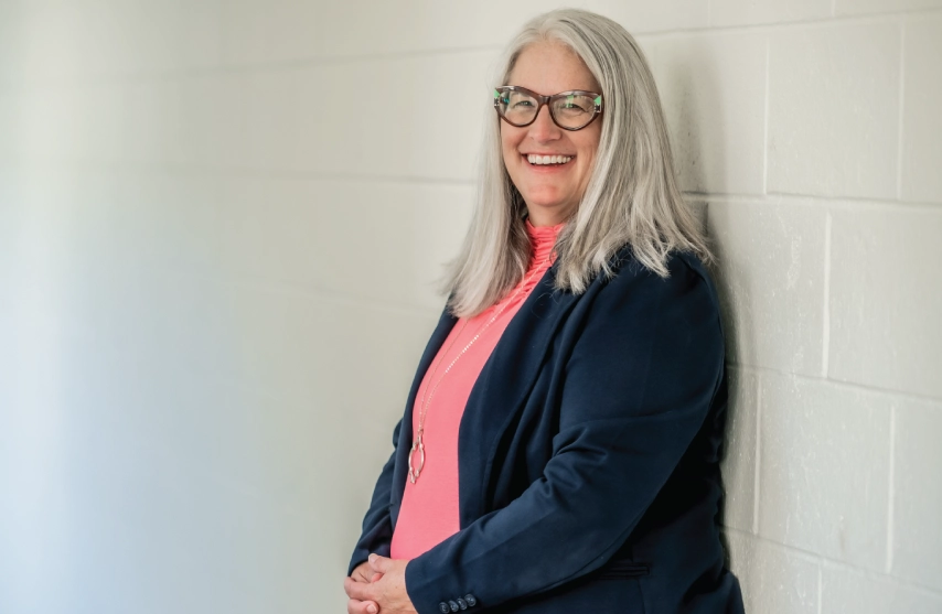Dr. Katie Van Blair smiling, while leaning against a white brick wall.