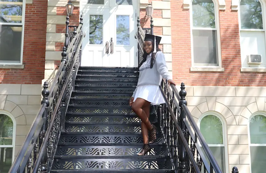 A student posing for a picture on the stairs to Ambrose Hall.