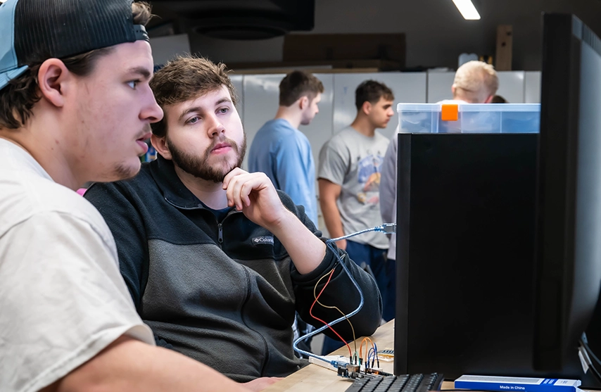 Students work together at a computer, testing electronics connected to a desktop workstation