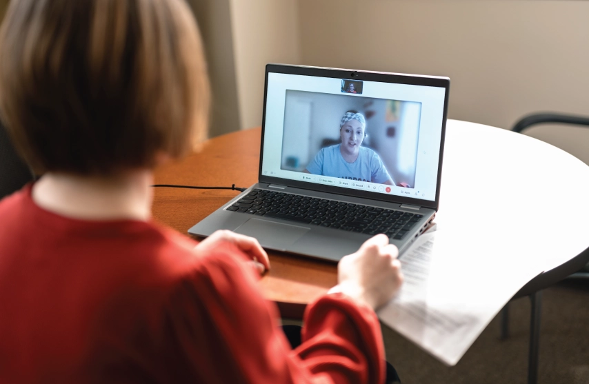 A woman sitting on zoom speaking with another person.