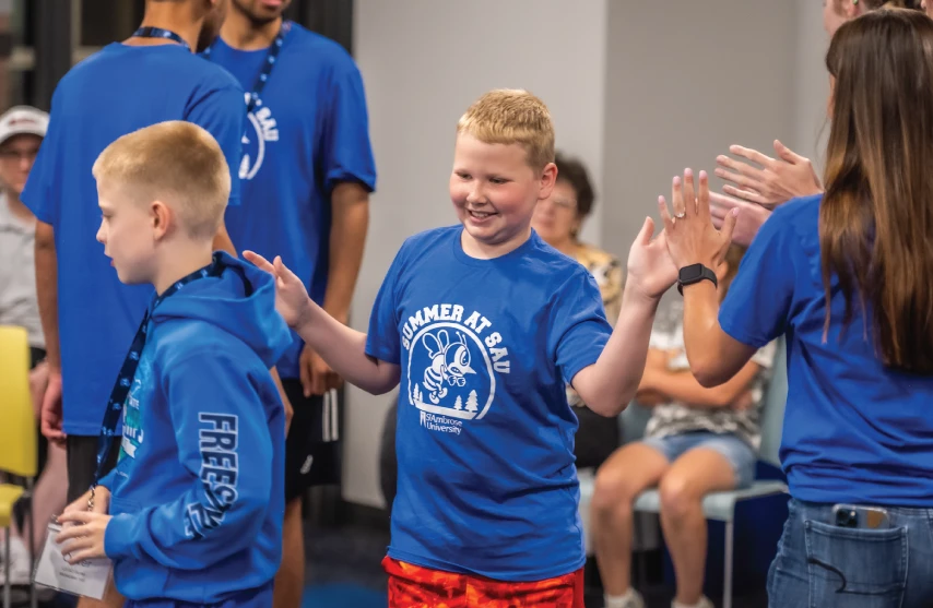 Children in blue St. Ambrose summer camp shirts high-five counselors