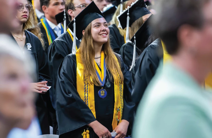 Graduate smiling and looking ahead in cap and gown with cords and medal.