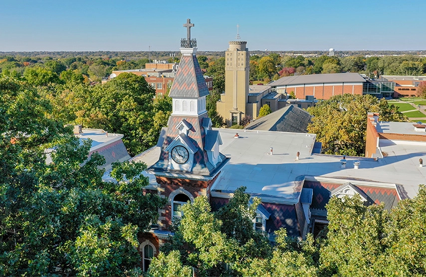 An outdoor aerial view of Ambrose Hall during the summertime, surrounded by green trees.
