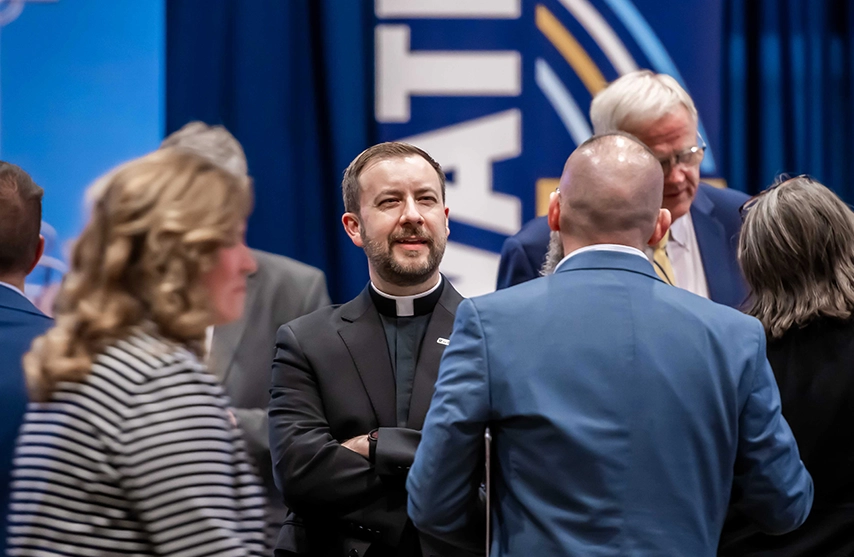 Father Thomas J. Hennen, '00, faces the camera as he talks with fellow alumni who face away from the camera.