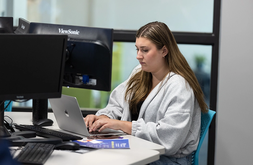 A student faces a computer and monitor.