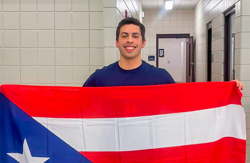 Khalil Ruiz smiles into the camera as he holds up the Puerto Rican flag.