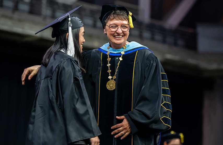Amy Novak, EdD, smiles in formal graduate regalia with a recently graduated student.