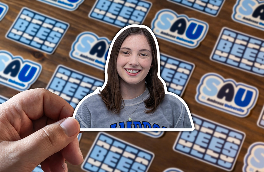 A sticker of Evelyn Shaw against a tile backdrop of blue and white SAU branded stickers.