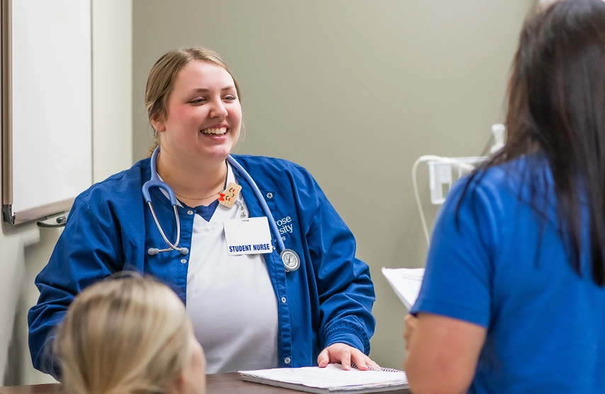A student nurse practices with another student while both were blue scrubs.