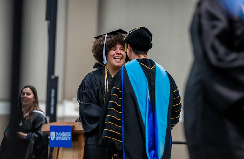 A student smiles as she receives her degree at St. Ambrose University.