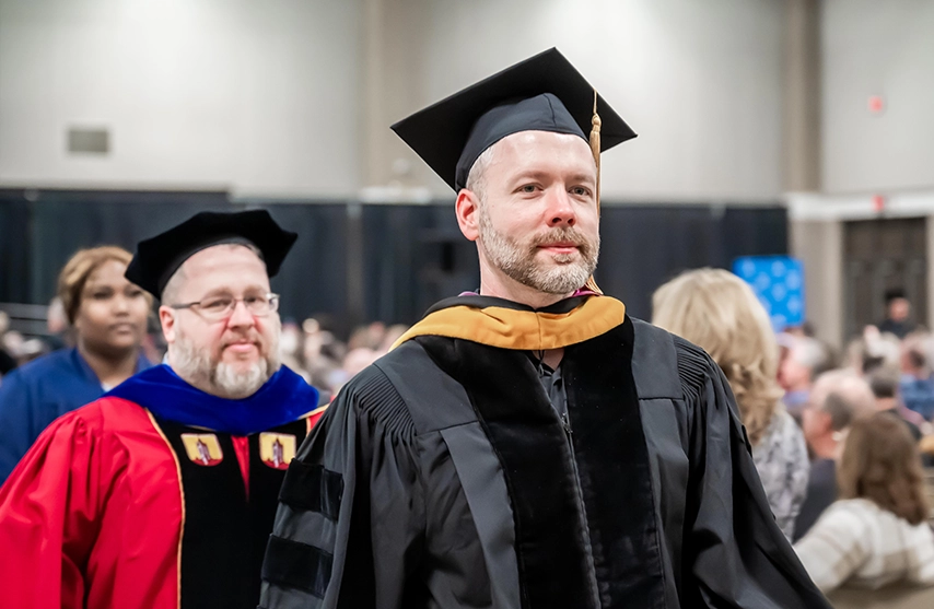 Professors in full commencement regalia walk to the stage.