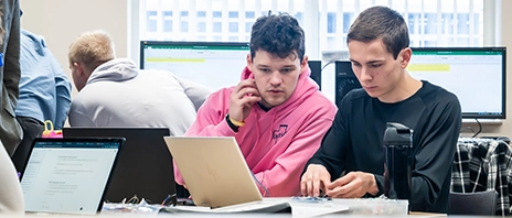 Students working on computer and electronics projects in a classroom lab.