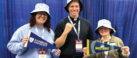 Three individuals smiling in bucket hats, with pennant flags for SAU and MMU.