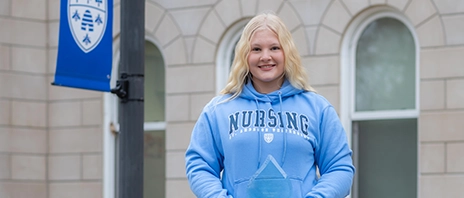Brenna Teerlinck holds her National Blood Donation Hall of Fame award and smiles at the camera.