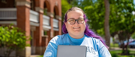 Jennifer Parsons smiles into the camera while holding her laptop on St. Ambrose University's campus.
