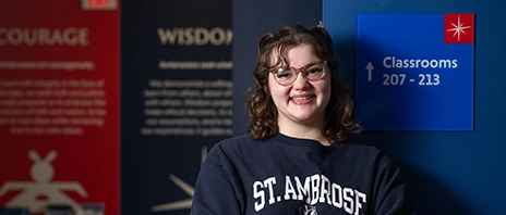 Madelyn Reum, '29, smiles into the camera against a background of the SAU values.