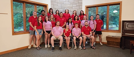 A group of Campus Ministry students from both St. Ambrose and Mount Mercy University campuses smile for a photo in front of a fireplace.