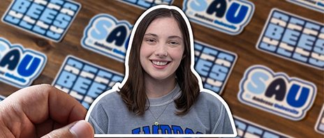A sticker of Evelyn Shaw against a tile backdrop of blue and white SAU branded stickers.
