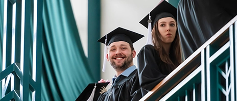 Students stand at the balcony and smile down at the camera during St. Ambrose University's graduation.