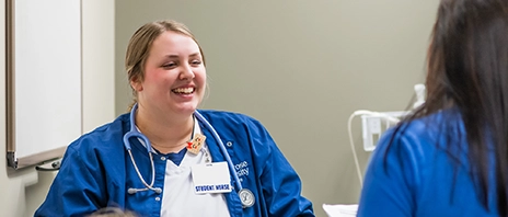 A student nurse practices with another student while both were blue scrubs.