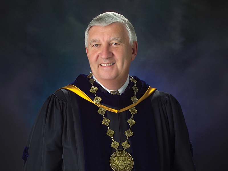 Dr. Edward Rogalski smiles into the camera while wearing the Presidential garb of St. Ambrose University.