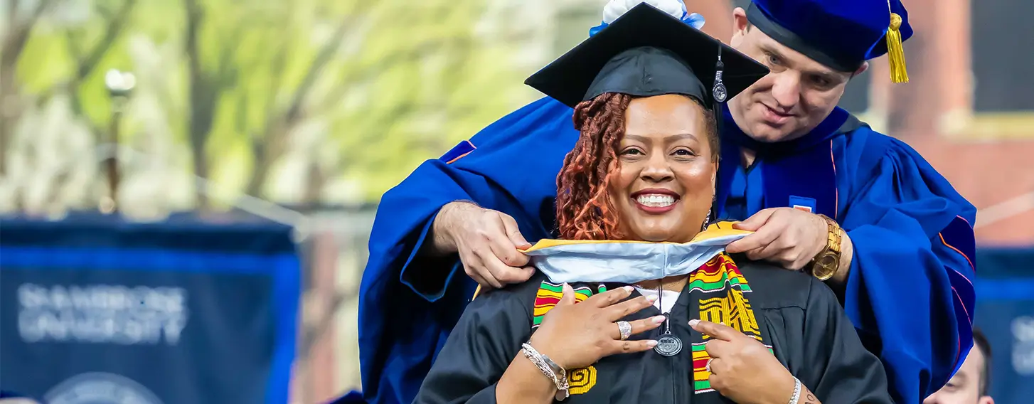 A smiling woman in a graduation cap and gown getting her masters hood.