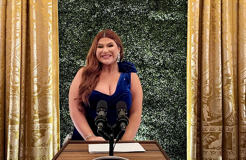 Briana Morales stands in front of a grass wall in a black dress.