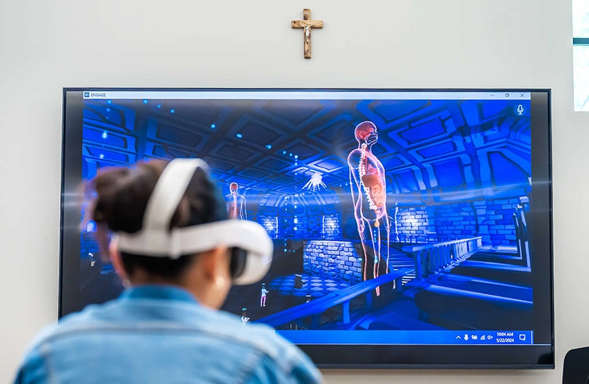 A student uses a VR headset while a tv projects the virtual digestive system of a human.