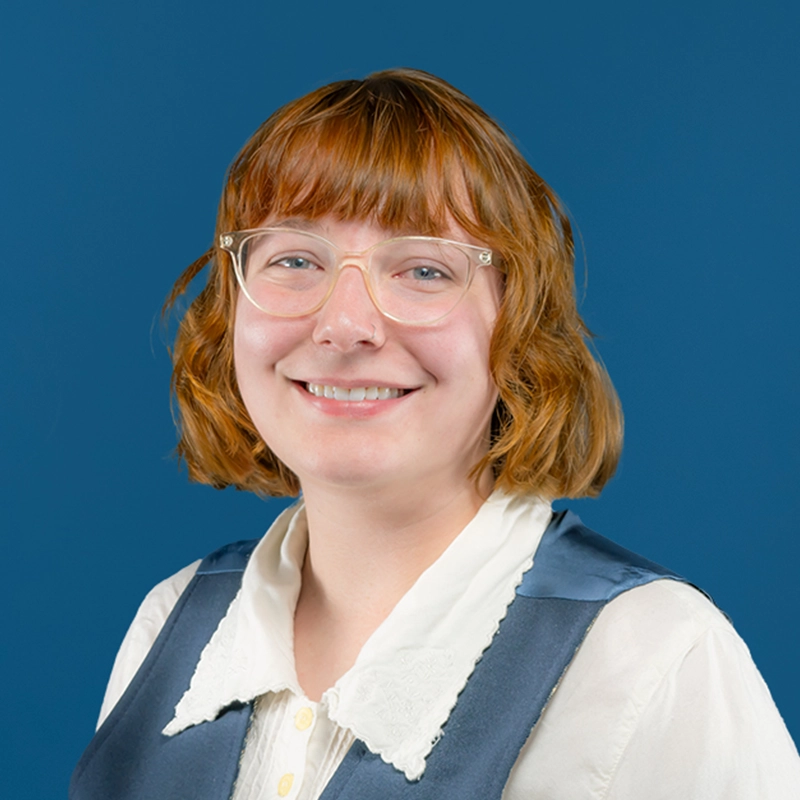 Communications and Marketing Specialist Aubrey Lathrop smiles into the camera against a blue background.
