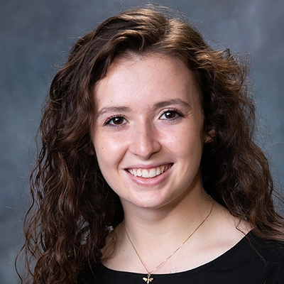 Hayley Coker smiles into the camera against a blue-gray background.