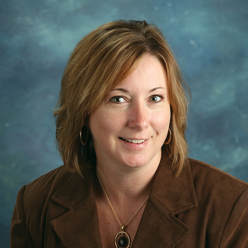 Lori Maher smiles at the camera against a blue background.