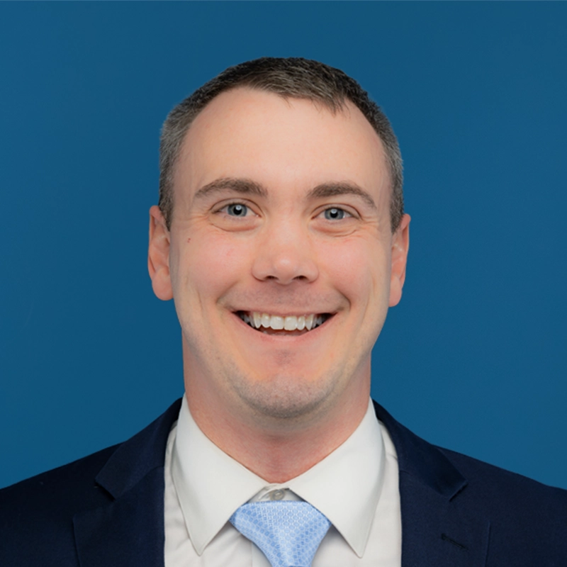Ryan Leabo smiles at the camera against a blue background.